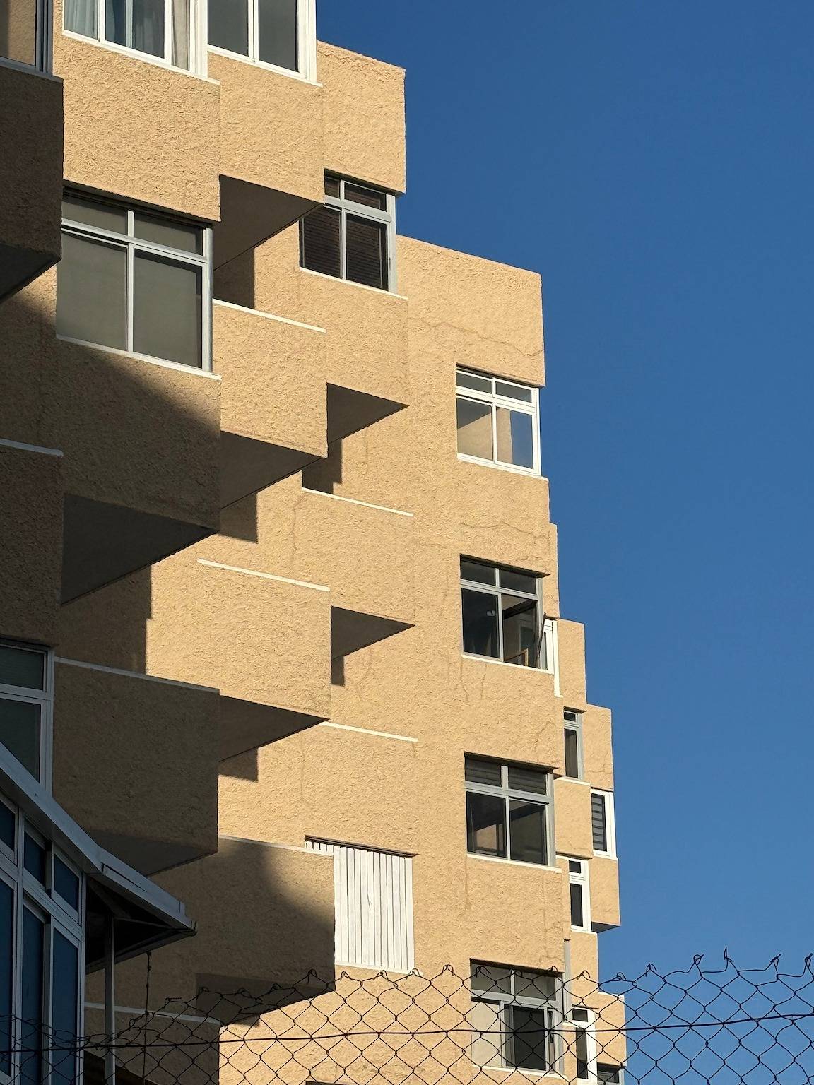 Sand-coloured facade with stepped windows against a blue sky